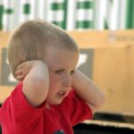 Małe dziecko zasłania uszy rękami w hałaśliwym otoczeniu miejskim z samochodami