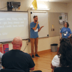 Uśmiechnięta grupa dzieci i rodzeństwa z instruktorką na warsztatach migowych