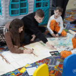 Arteterapia dziecięca - jak pędzel i kredka pomagają maluchom oswajać emocje i budować pewność siebie? Grupa dzieci maluje kolorowe obrazy pod okiem terapeuty w jasnym atelier