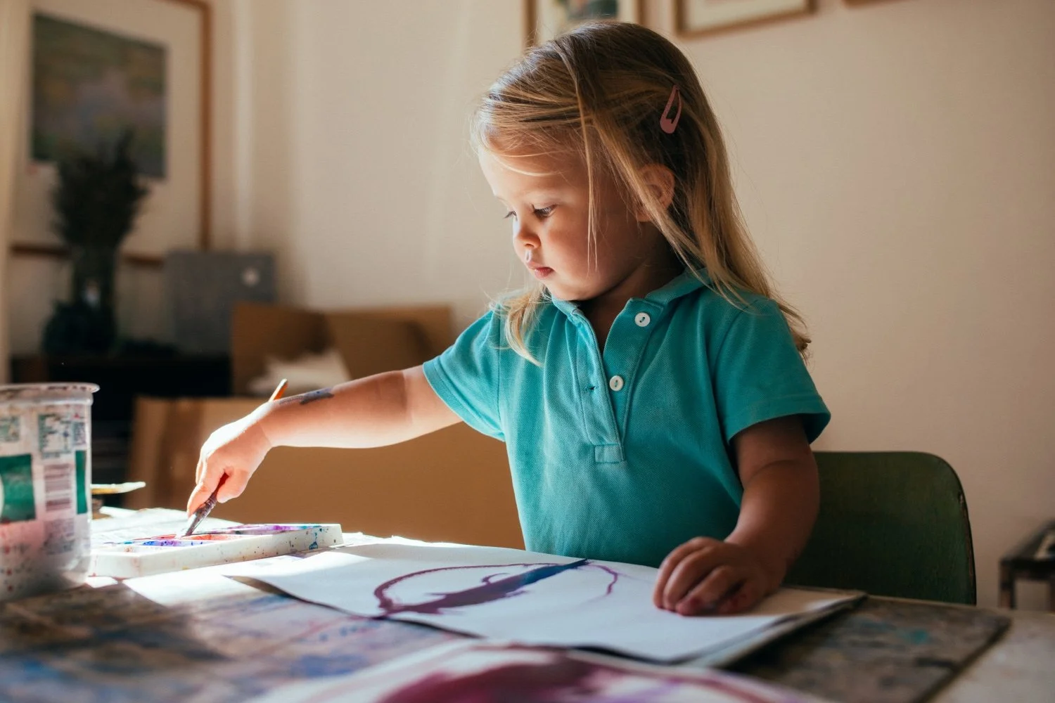 Chłopiec miesza farby palcowe tworząc chaotyczny tęczowy wzór na dużym papierze