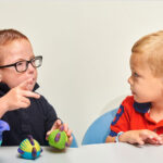 dziecko głuche uśmiechnięte komunikujące się migowo z terapeutą w gabinecie